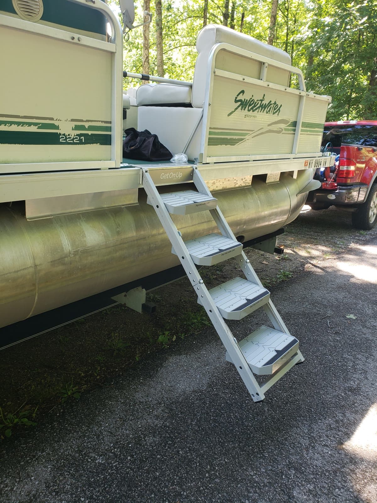 The nautiDAWGS ladder mounted on the stern of a Sweetwater pontoon boat, deployed while the boat sits on its trailer